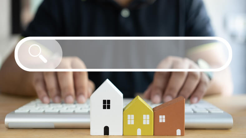 image représentant une barre de recherche située au-dessus de trois immeubles colorés, des mains sur un clavier sont visibles derrière, représentant la recherche d'appartement étudiant Paris