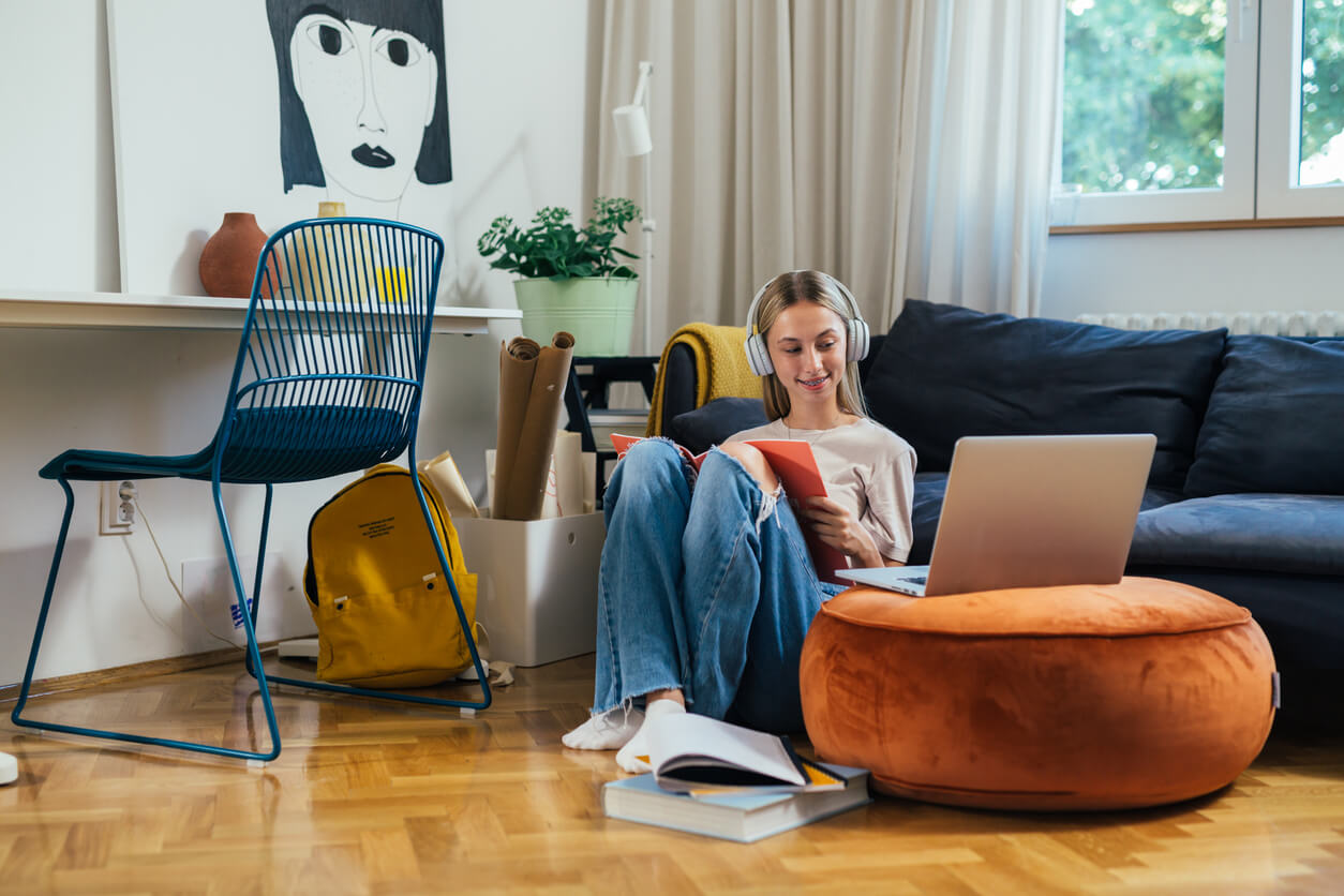 Une jeune étudiante est assise dans son salon, écoutant un casque et travaillant sur son laptop. Elle se trouve dans un beau logement, semblable à ceux disponibles en location étudiant dans Paris 18.